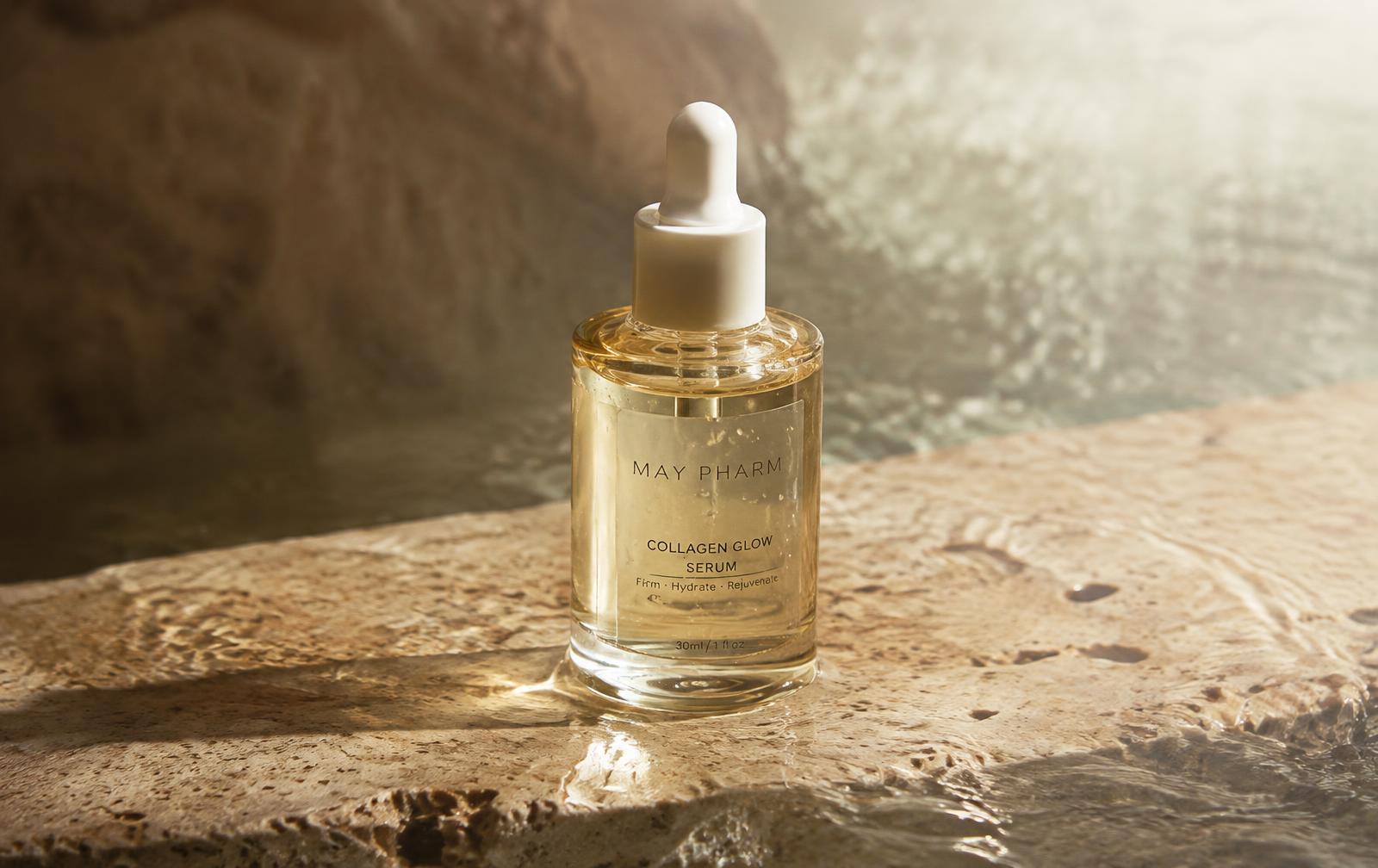 May Pharm Collagen Glow Serum bottle on wet travertine stone in morning light